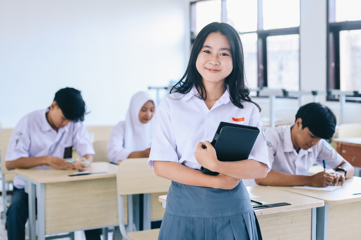 High school student holding books and looking at camera in classroom.