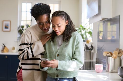 Happy mom looking over happy daughters shoulder at her phone