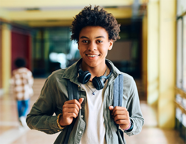 Smiling high school student wearing a backpack and headphones in a school hallway